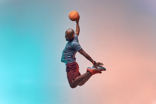 Slam dunk per tutta la lunghezza del giovane giocatore di backetball africano che salta su sfondo colorato