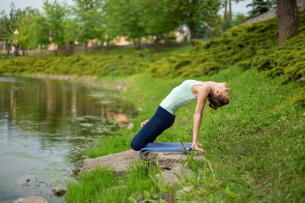 Slank donkerbruin meisje dat yoga in de zomer op een groen gazon doet