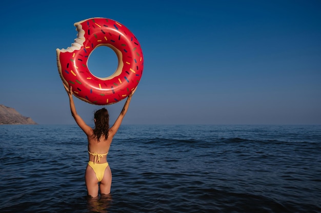 Slank meisje met een sexy buit in een zwempak houdt een opblaasbare cirkel in haar handen op een zonnige zomerdag aan zee