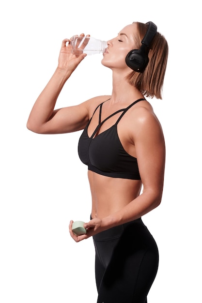 Slanke aantrekkelijke vrouw in sportkleding met handdoek drinkt water na training op witte geïsoleerde background