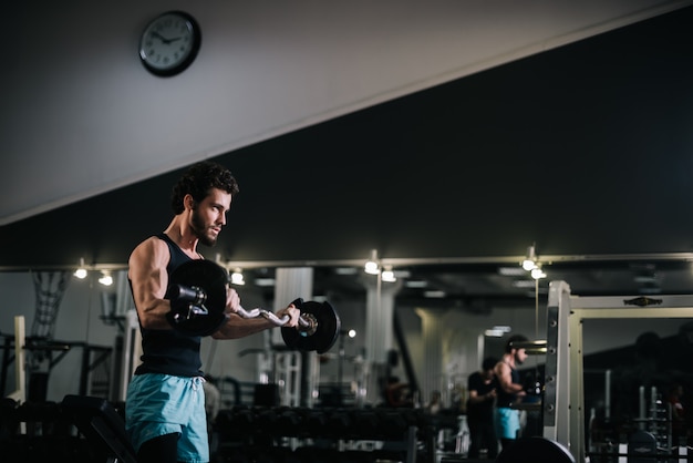 Slanke, bebaarde jonge man met gespierd, stug lichaam die sportkleding draagt die halter opheft