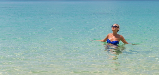 Slanke blondevrouw die op tropisch strand zwemmen