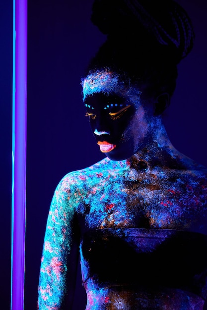 Slanke fascinerende zwarte vrouw met neon body art met fluorescerend poeder poseren