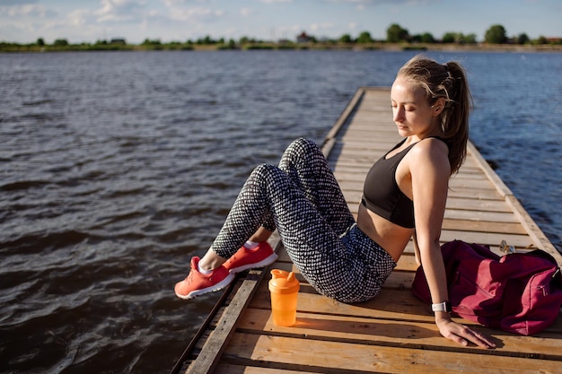 Slanke fitness vrouw zitten en ontspannen na trainingen op de pier bij zonsondergang