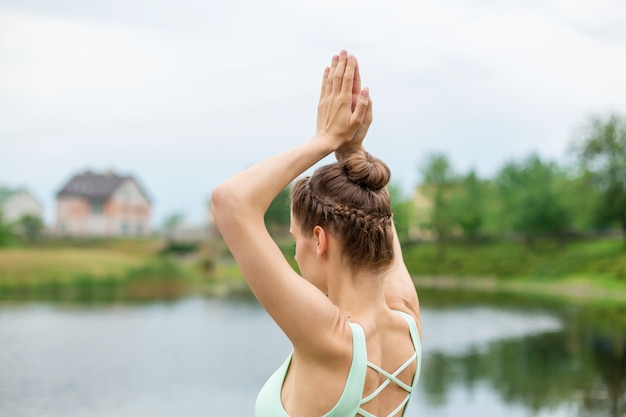 Slanke jonge brunette yogi voert geen ingewikkelde yoga-oefeningen op het groene gras in de zomer uit tegen de natuur