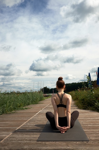 Foto slanke jonge vrouw beoefenen van yoga op de houten pier in de buurt van meer.