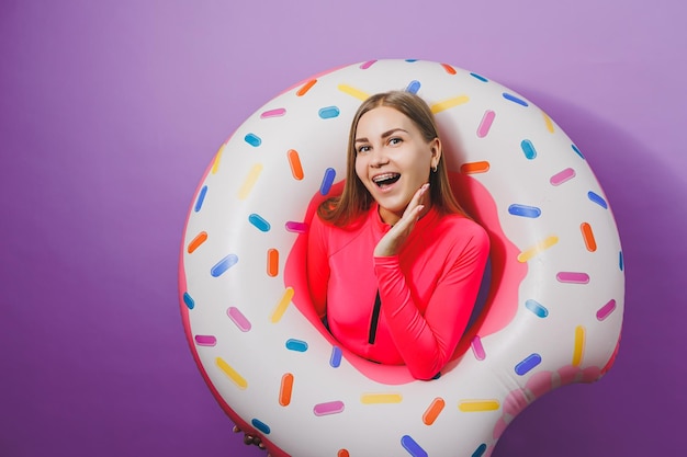 Slanke jonge vrouw in een stijlvol roze zwempak met een opblaasbare ring van donut op een effen achtergrond