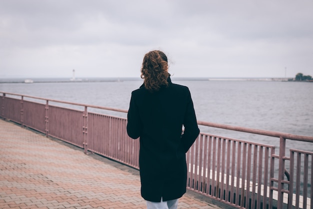 Slanke jonge vrouw in een zwarte jas loopt