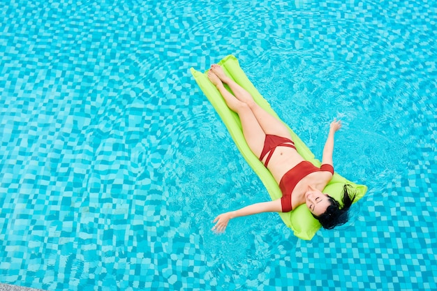 Slanke jonge vrouw in rode bikini ontspannen op opblaasbare matras drijvend in zwembad van kuuroord