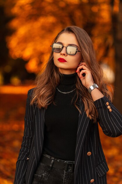 Slanke jonge vrouw professional in modieuze sportkleding in sneakers staat op de weg tussen de bomen in het park. Aantrekkelijk meisje met mooi atletisch lichaam houdt zich bezig met fitness buitenshuis bij zonsondergang.