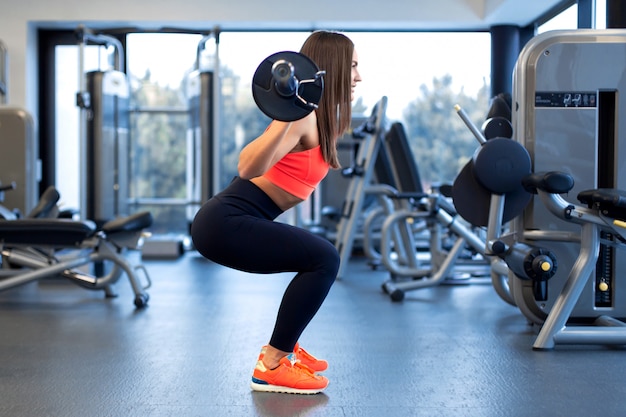 Slanke knappe jonge vrouw in sportkleding squats met een halter op de schouder in de sportschool