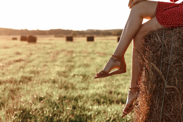 Slanke mooie benen van een jonge vrouw zittend op een hooiberg in een veld bij zonsondergang