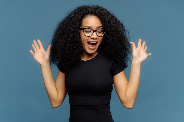 Slanke overemotive donkere vrouw heft handen op, opent mond, gebaren actief van positieve emoties