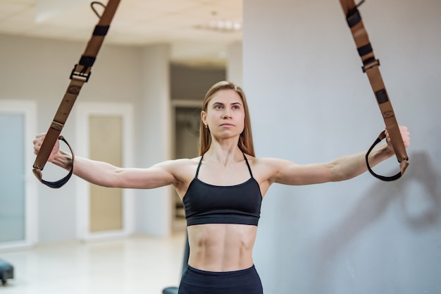 Slanke vrouw in gym training armen met trx fitness strips.