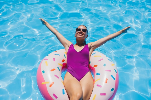 Slanke vrouw met zonnebril in het zwembad in een opblaasbare zwemring in een helder badpak zomerfoto zwemfotografie zomervrouwenfoto's Strandmode