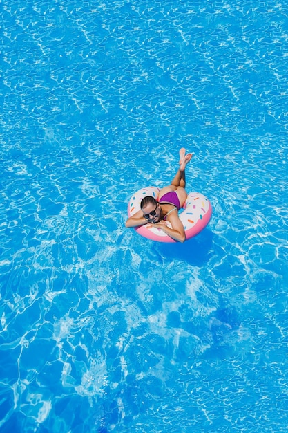 Slanke vrouw met zonnebril in het zwembad in een opblaasbare zwemring in een helder badpak zomerfoto zwemfotografie zomervrouwenfoto's Strandmode