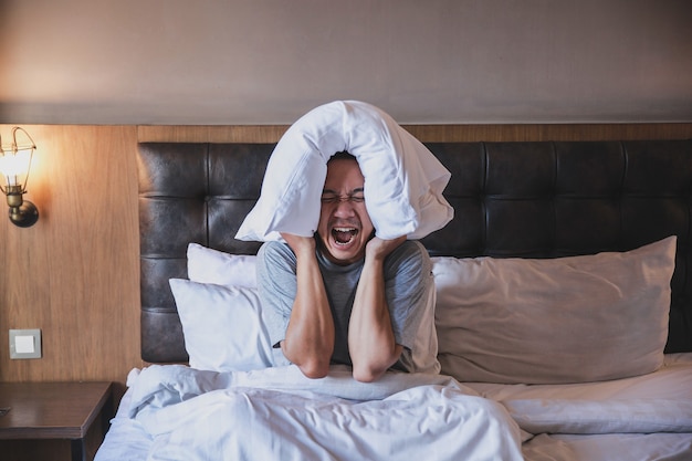 Slapeloosheid man schreeuwen gestoord met het bedekken van zijn oren gebruik een kussen op een bed