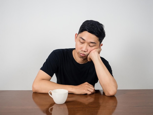 Slapeloze man zit 's ochtends aan tafel te slapen met een koffiekopje