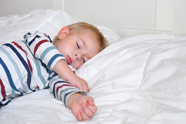 Slapend kind in bed. Schattige kleine jongen slaapt zoet op een gezellige witte deken op zijn kant. 2 jaar oud kind slapen in wieg. Gezichtsclose-up. Jonge jongen liggend in bed op kussen tijdens de dagslaap. 4K
