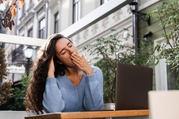 Slapend meisje met laptop geeuwt buiten op terras in café Moe jonge vrouw heeft een pauze op het werk en slaapt en ontspant op laptop op werkplek vanwege overwerk