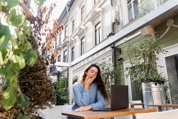 Slapend meisje met laptop geeuwt buiten op terras in café Moe jonge vrouw heeft een pauze op het werk en slaapt en ontspant op laptop op werkplek vanwege overwerk