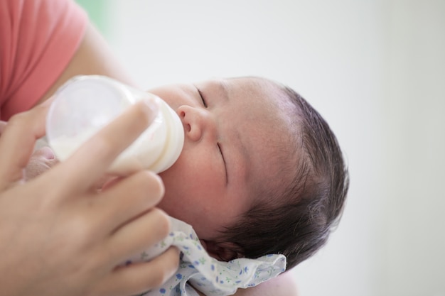 Slapend pasgeboren babymeisje die een melk van fles in de wapens van haar moeder drinken