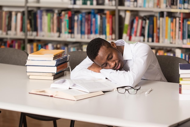 Slapende Afrikaanse student zittend en leunend op stapel boeken op de universiteit Ondiepe scherptediepte