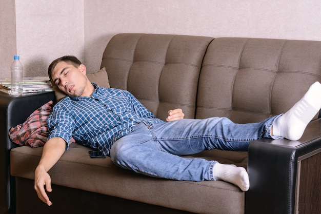 slapende jonge man op de bank in de kamer, moe na het werk, dronken na een feestje.