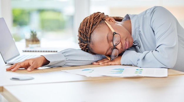 Slapende moe of burn-out zwarte vrouw in financieel kantoor met bureaulaptop of infographic documenten Uitgeput overwerkt of depressie voor boekhoudkundige nalevingsmedewerker in financiële auditzaken