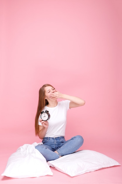 Slaperig meisje probeert wakker te worden met wekker op roze achtergrond