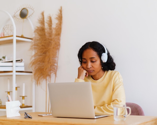 Slaperige Afro-Amerikaanse vrouwelijke student met koptelefoon die thuis online lezing op laptop bijwoont