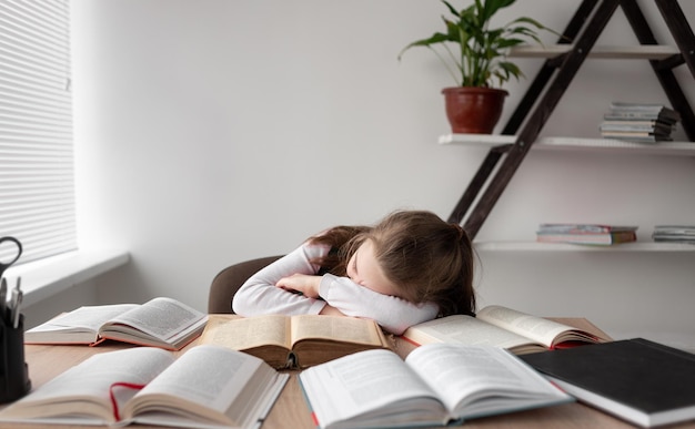 Slaperige, vermoeide ongemotiveerde student die aan een bureau ligt met open boeken die het materiaal van verschillende lessen tegelijkertijd bestudeert slim kinderwonderkind leest literatuur terwijl hij thuis online studeert