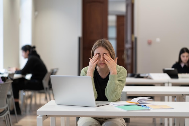 Foto slaperige, vermoeide volwassen vrouwelijke student die zich uitgeput voelt na lange uren in de bibliotheek te hebben gestudeerd