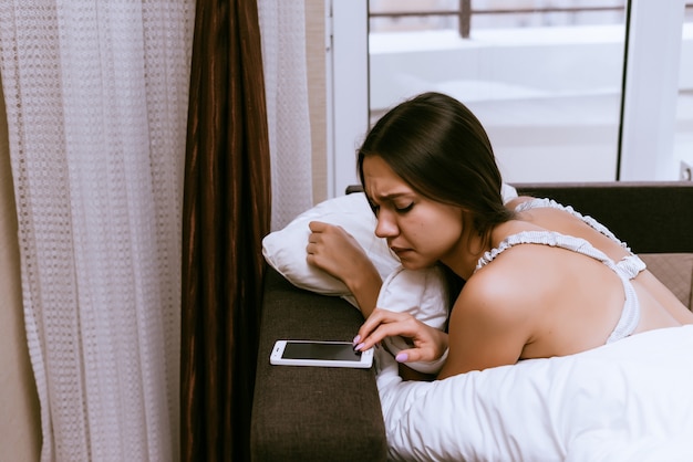 Slaperige vrouw ligt in bed en kijkt in de telefoon