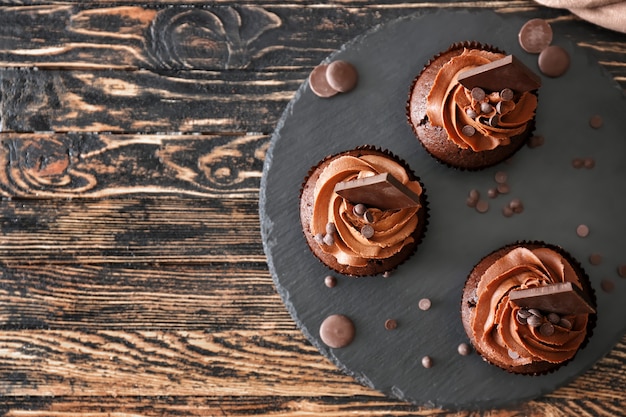 Slate plate with tasty chocolate cupcakes on wooden table