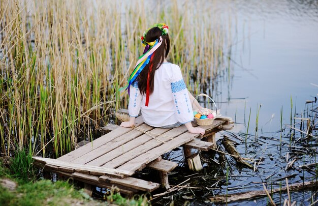 Slavic girl in ukrainian shirt sitting on the bridge with easter