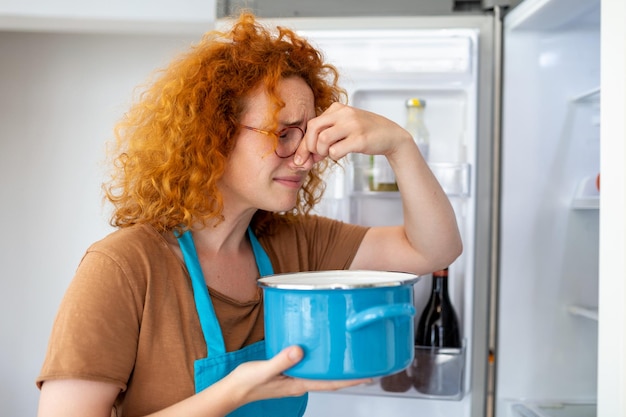 Slecht voedsel in de koelkast jonge vrouw houdt haar neus dicht vanwege de slechte geur van voedsel in de koelkast thuis