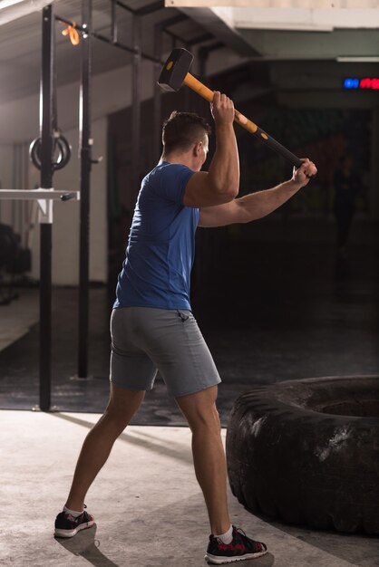 Sledgehammer tire hits jonge gespierde man training in sportschool met hamer en tractorband