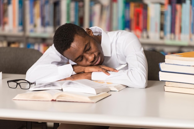 Sleeping African Student Sitting And Leaning On Pile Of Books In College  Shallow Depth Of Field