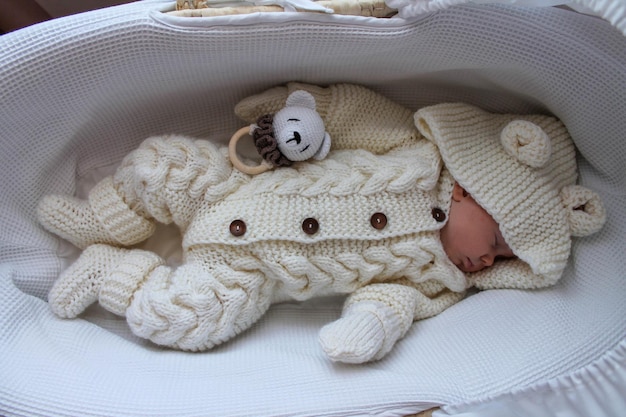 Sleeping baby girl in a white knitted suit lies in her white crib