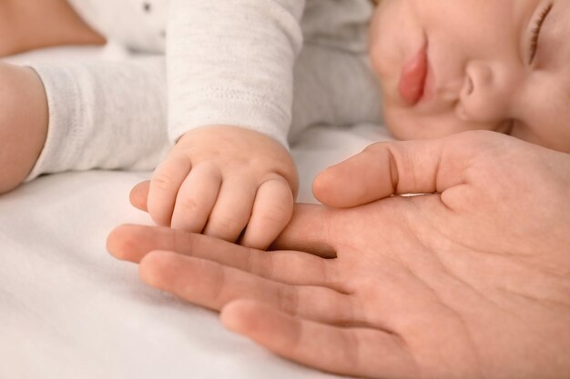 Sleeping baby holding mother's hand on bed