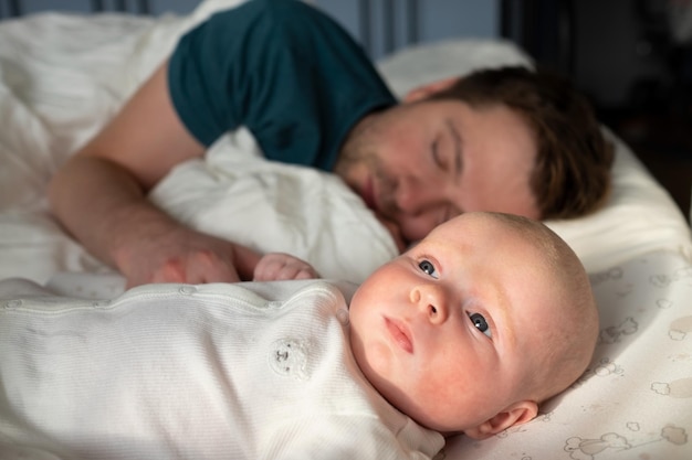 眠っている父とかわいい子供が一緒にベッドで休んでいます。