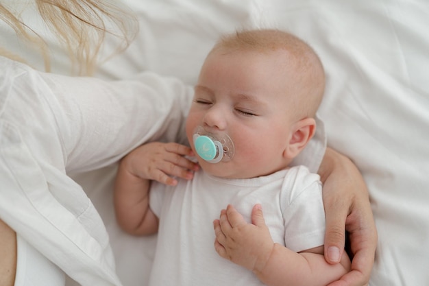 Photo sleeping four months baby boy on white bed linen in minimalistic bodysuit face closeup portrait