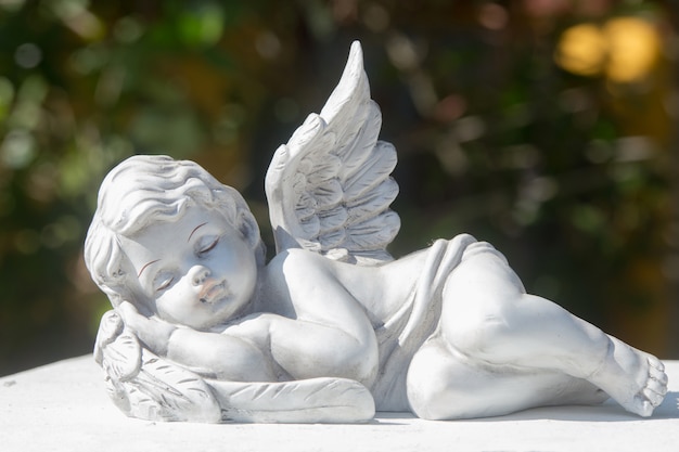 Sleeping of little cupid's ceramic doll on stone. Items for house, garden, and interior