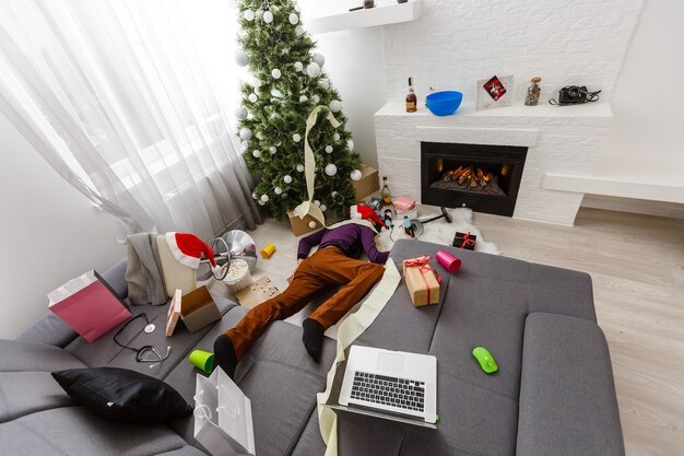 Спящий мужчина на диване после рождественской вечеринки.