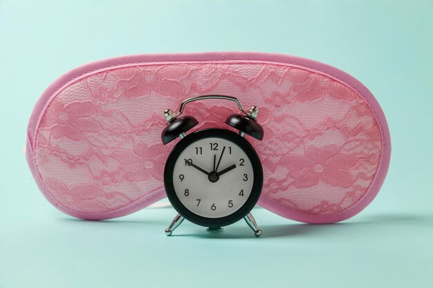 Sleeping mask and alarm clock on blue background