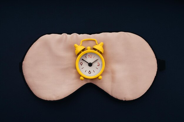 Sleeping mask and yellow alarm clock on dark blue background