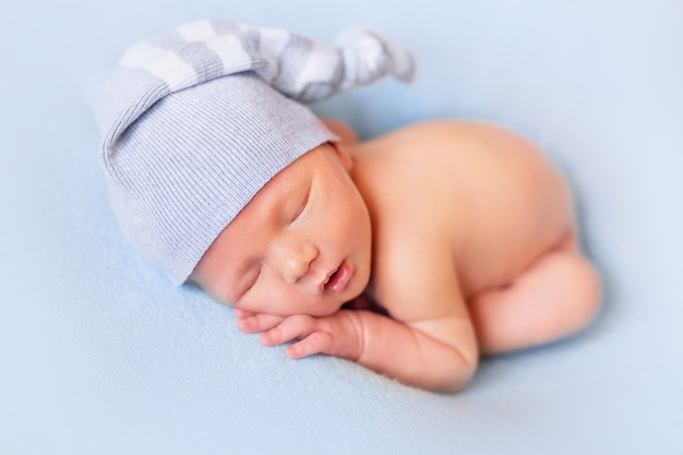 Sleeping newborn baby on the blue bed. Child in a nightcap