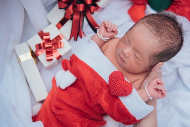 Sleeping newborn baby on mother hand in Christmas hat with gift box from Santa Claus 