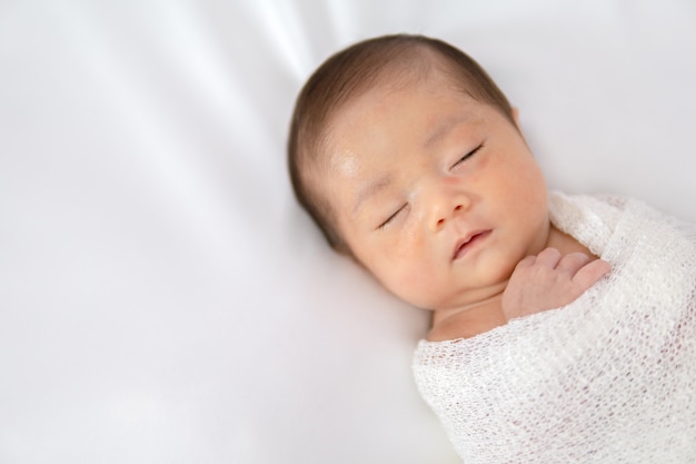 Sleeping newborn baby in white wrap while on white blanket background. 